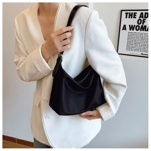 Close-up of a sleek black nylon hobo tote bag worn with a white blazer for a modern look