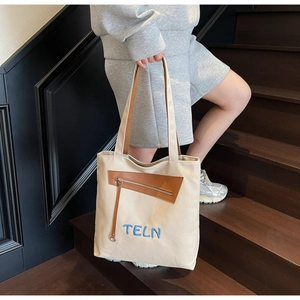 Détail du sac cabas en toile avec broderie TELN et finitions en cuir marron sur escalier
