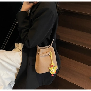 Close-up of lychee grain bucket bag in khaki with a cute yellow duck charm on stairs