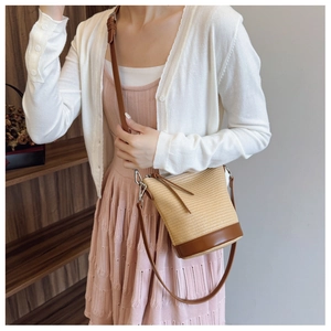 Detail of woven bucket bag with brown leather base and adjustable crossbody strap