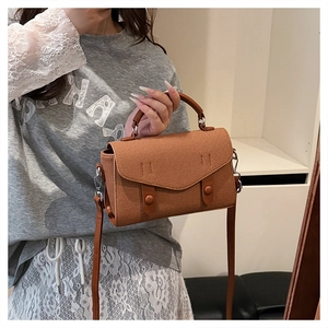 Detail of a brown textured canvas and leather crossbody bag with top handle and strap