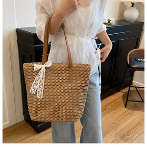 Detail of hand-woven straw tote bag featuring leather handles and delicate lace bow