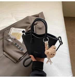 Gros plan d'un sac à main en cuir grainé noir avec un ours en peluche et ruban coloré