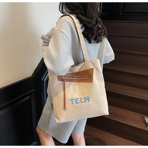 Détail du sac cabas en toile beige avec empiècement en cuir brun et broderie TELN