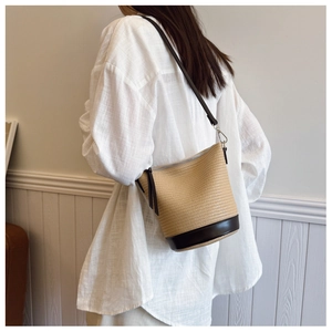 Detail of hollow straw bucket bag featuring a brown leather base and slim shoulder strap