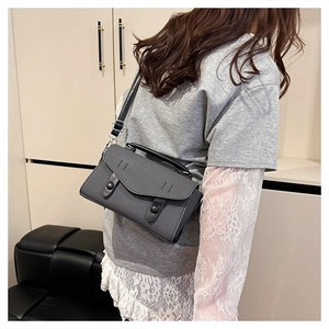 Gray structured crossbody bag with top handle and black button on model for size scale