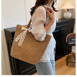 Close-up of woven straw tote bag featuring white lace bow detail and brown leather handles