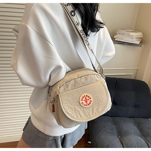 Close-up of beige nylon crossbody bag featuring wide logo strap and multi-pocket detail