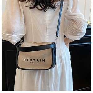 Detail of minimalist beige canvas crossbody bag with black leather trim and metal buckles