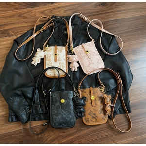 Detail view of four color teddy bear crossbody phone bags on a leather jacket background