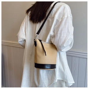 Detail of woven straw bucket bag with black leather base and shoulder strap on model