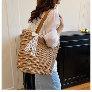 Detail of large woven straw tote with delicate white lace bow and brown leather straps