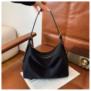 Detail of black nylon tote bag with metal zipper and adjustable leather strap on a vintage chair