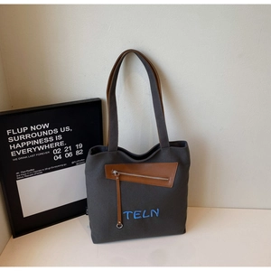 Détail du sac en toile grise avec finitions en cuir marron et broderie TELN bleue