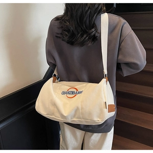 Détail du sac bandoulière en toile avec logo brodé et accents en cuir marron