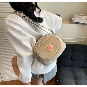 Detail of beige square crossbody bag with red logo embroidery and branded woven strap