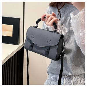 Detail of medium grey textured leather bag with black decorative straps and flap closure