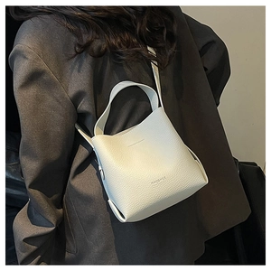 Crossbody view of white lychee pattern bucket bag on a professional grey blazer model
