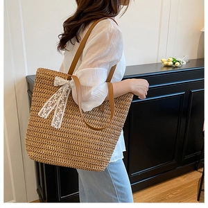 Detail of hand-woven straw tote with elegant white lace bow and brown leather handles