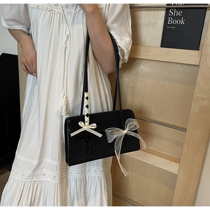 Detail of black glossy shoulder bag featuring delicate rib ribbon and organza bows