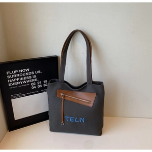 Détail du sac cabas en toile gris foncé avec poche zippée en cuir marron et broderie bleue