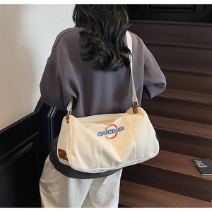 Détail du sac bandoulière en toile crème avec broderie bleue et finitions en cuir marron