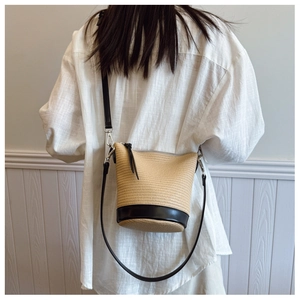 Close-up of woven straw bucket bag with black leather trim and adjustable crossbody strap