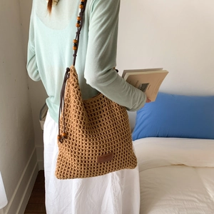 Detail of hollow woven beach tote featuring rope straps and decorative wooden beads