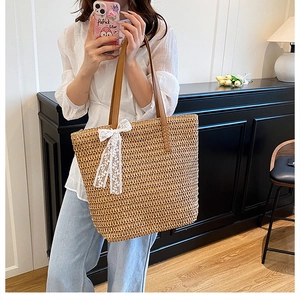 Detail of hand-woven straw tote with brown PU straps and a white lace bow charm