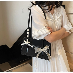 Detail of black glossy shoulder bag with large white mesh bow and ribbon strap details