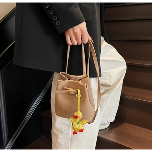 Close-up of brown litchi leather bucket bag featuring a cute yellow duck pendant