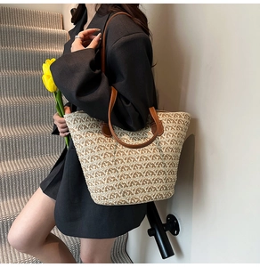 Dettaglio borsa tote in paglia intrecciata con spalline in pelle marrone tenuta da modella