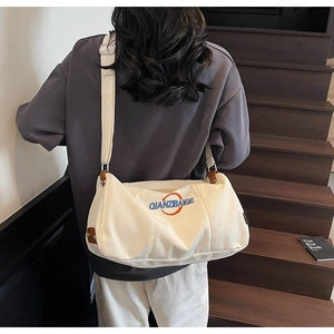 Vue détaillée du sac cabas en toile crème avec logo orange porté par un mannequin
