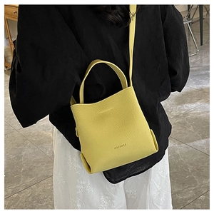 Close-up of bright yellow lychee pattern leather bucket bag held by a model with floral skirt