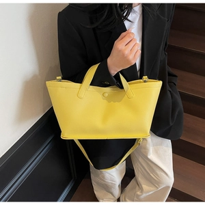 Detail of a bright yellow leather tote bag showing lychee grain texture and metal hardware