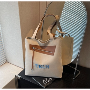 Détail du sac cabas en toile avec poche en cuir marron et broderie TELN bleue