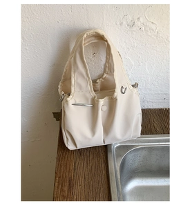 Detail of pleated beige fabric tote bag featuring silver metal accents and snap button closure