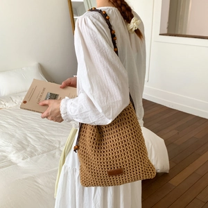 Detail of hollow-out hand-woven tote with wooden bead straps and a leather logo tag