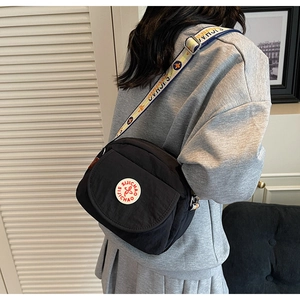 Close-up of black crossbody bag with wide logo strap worn by a model in casual style