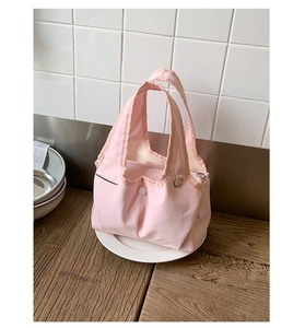 Detail view of pink nylon handbag featuring snap closure and metal ring on wooden table