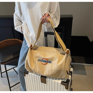 Vue détaillée du sac cabas en toile kaki avec poignée en cuir et logo sur une valise