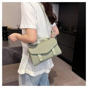 Detail of sage green textured crossbody bag with decorative buckles and flap closure