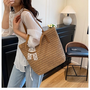 Detail of a woven straw tote bag with brown PU straps and a white lace bow accent
