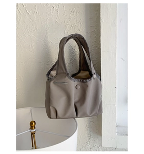 Detail showing taupe nylon handbag with round buckle decor and pleated bottom texture
