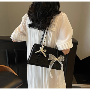 Close-up of glossy black shoulder bag with beige and organza bow detailing