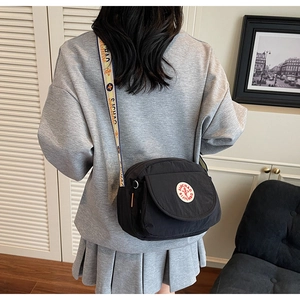 Detail of black nylon shoulder bag with wide printed strap and logo patch