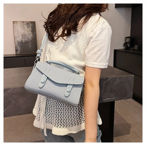 Side view of light blue textured shoulder bag with buckle straps and silver hardware