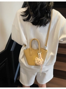 Sac seau jaune moutarde chic avec breloque ours présenté dans un cadre de vie urbain