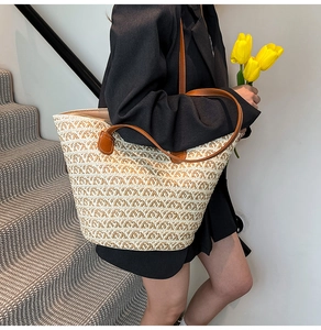 Dettaglio della borsa tote in paglia intrecciata con spalline in pelle marrone su modella
