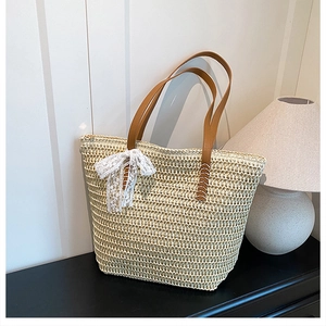 Close-up of beige woven straw tote bag featuring brown leather straps and lace bow